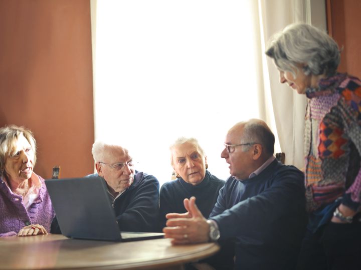 Grupo de adultos mayores conversando alrededor de una computadora