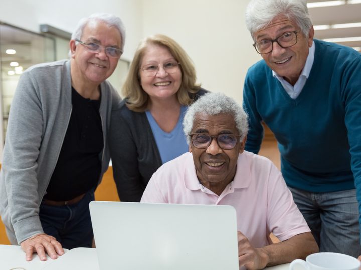 Amigos mayores sonriendo frente a una computadora